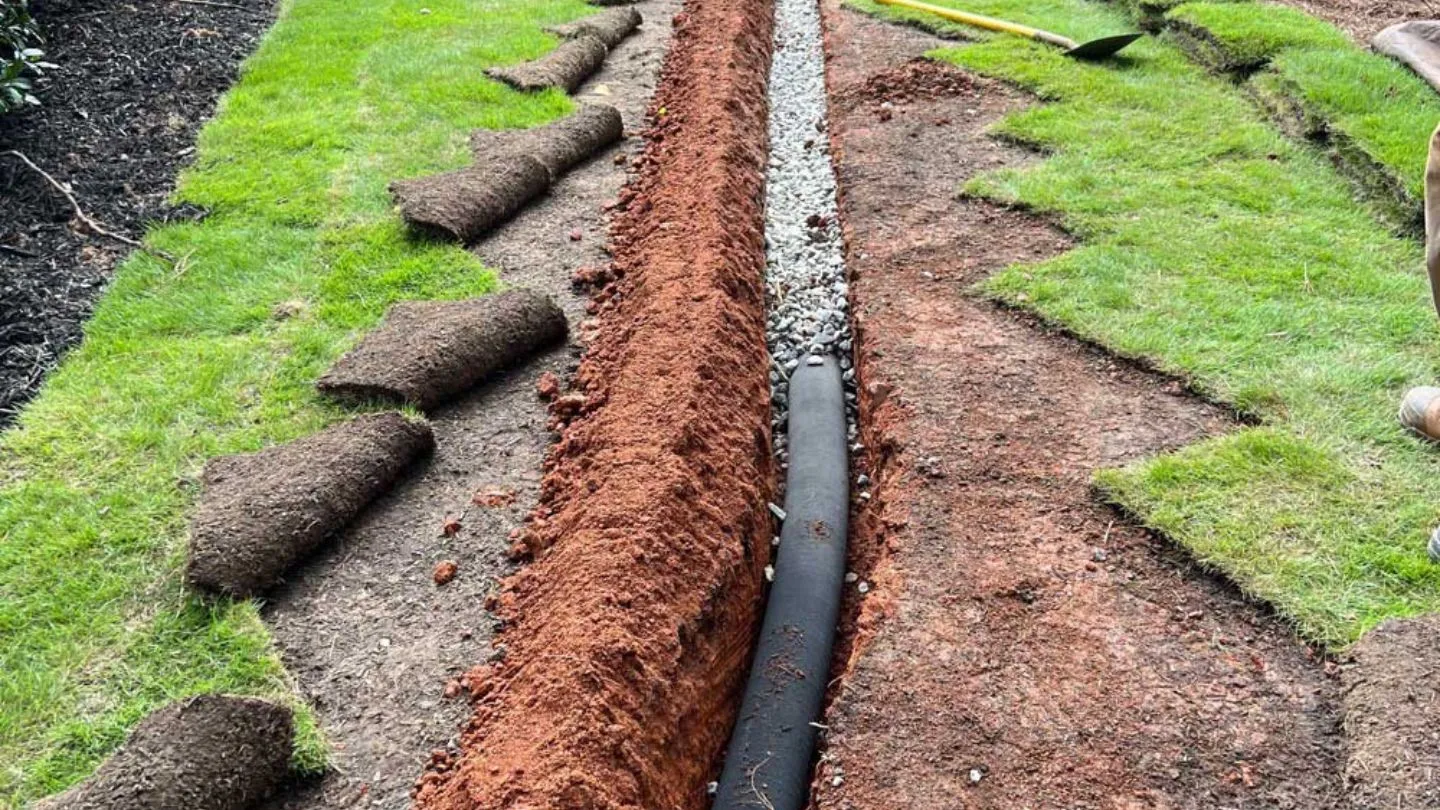 French drain trench with perforated pipe and gravel bedding beside a Fort Worth lawn