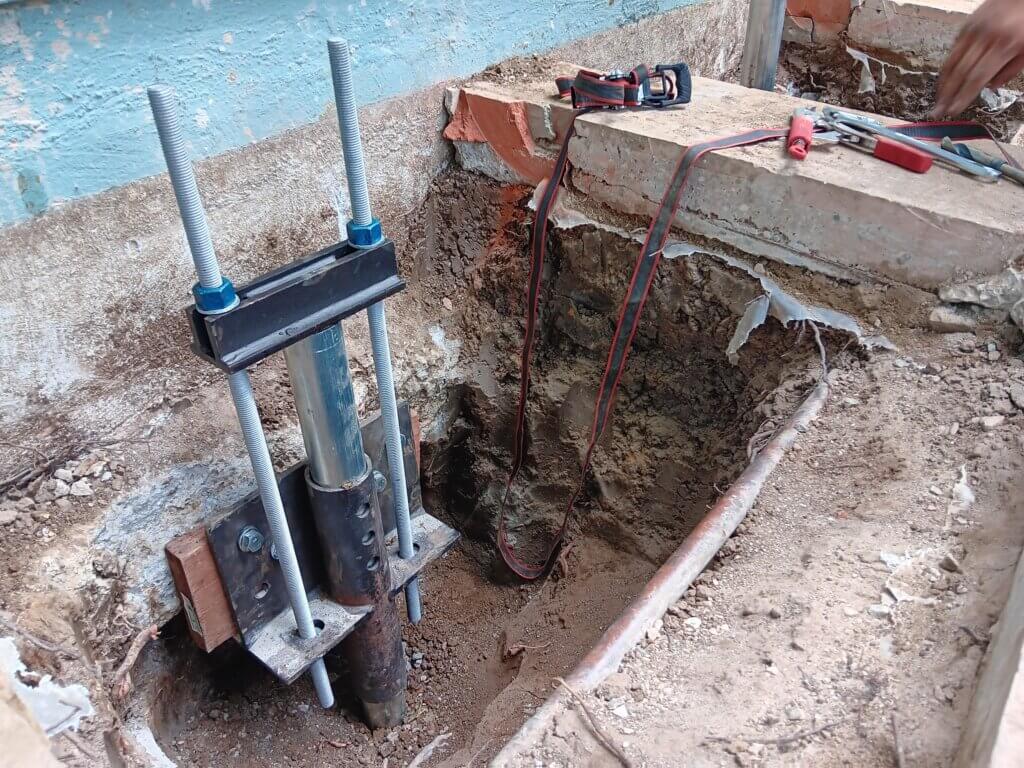 Hydraulic steel push pier jack installed beside a Fort Worth home's foundation wall